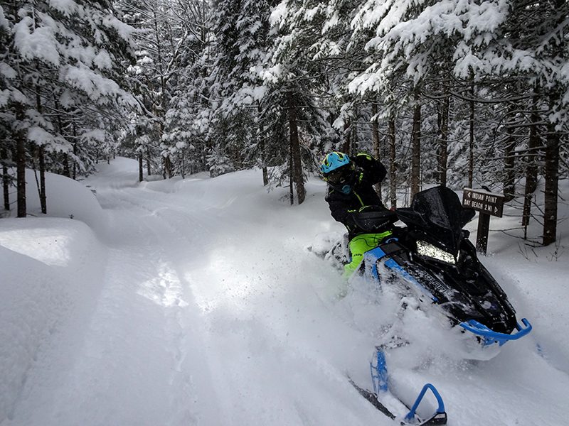 A person riding a snowmobile waves while riding along a snowy trail.