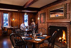 Two people dine in a warmly lit room with a fire roaring and warm wood throughout.