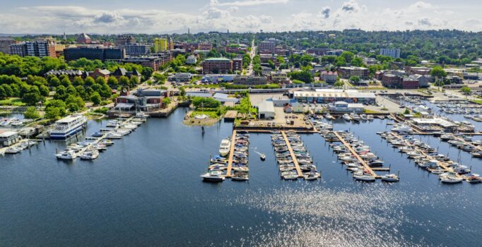 Seen from above, boats tied to docks extend into a large body of water on a warm sunny day.