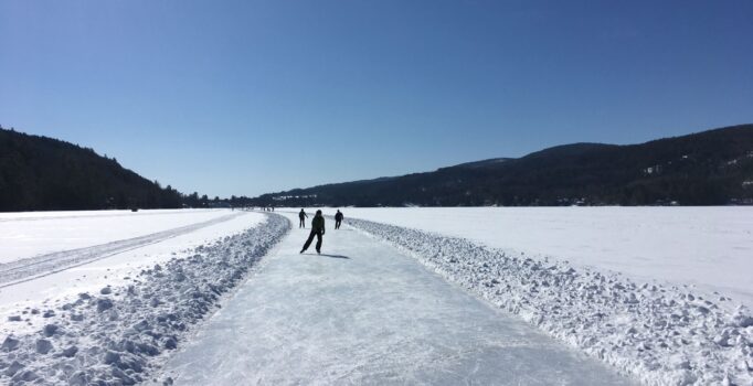 Three people ice-skate on a lake.