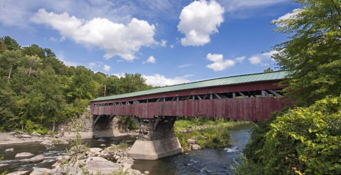 A red covered bridge with a green roof sits above a rocky river.