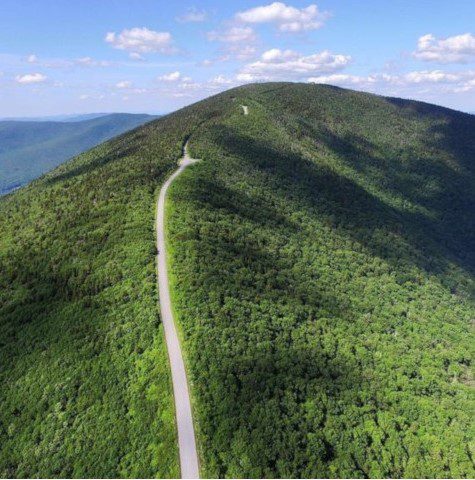 Seen from above, a narrow road goes to the top of a green, lush mountain.