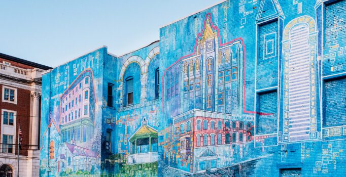 A painted mural on a wall of downtown buildings with a blue background.