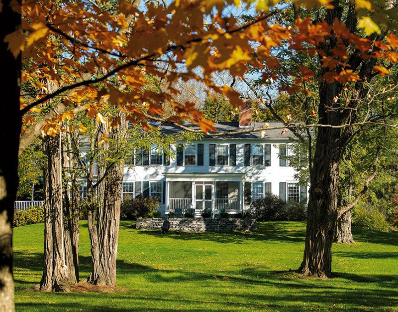 A white historic building is visible through trees with fall foliage.
