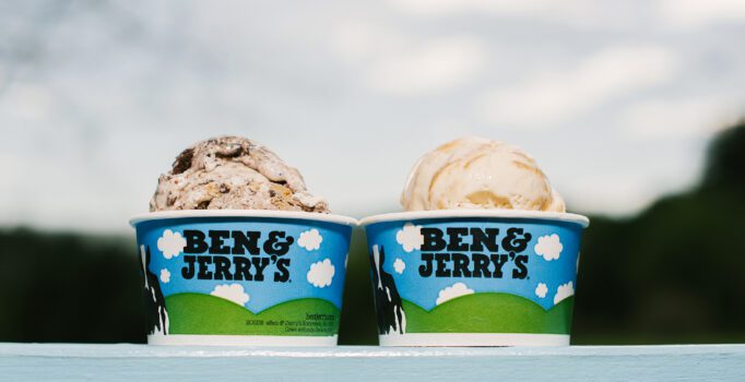 Two paper cups of ice cream that read Ben & Jerry's sit on a table.