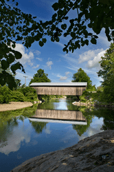 A wooden covered bridge spans a river on a sunny day.