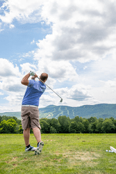 A person swings a golf club at a golf course on a sunny day.