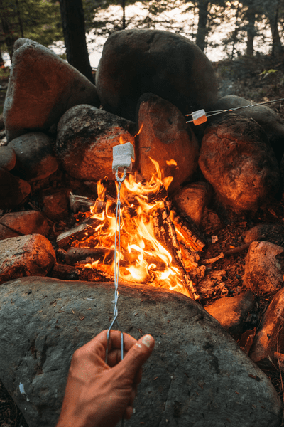 A marshmallow is on a cooking fork over a camp fire.