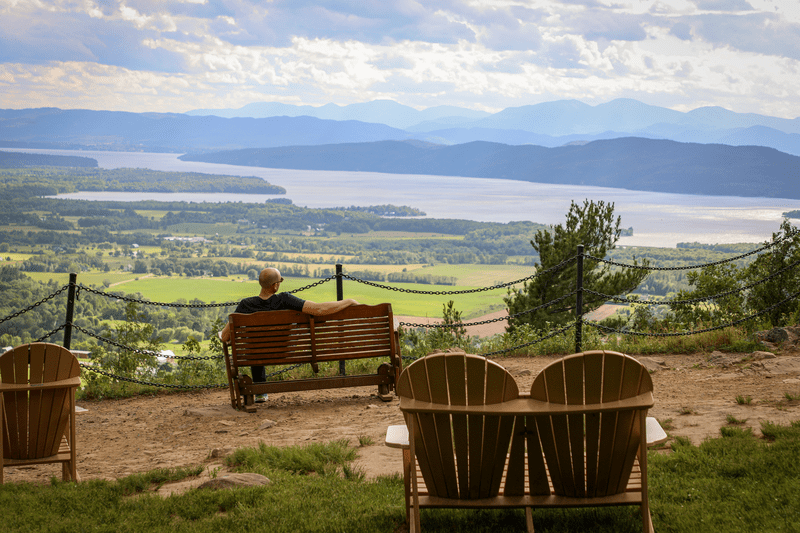 A person sits on a chair on a hill looking at the view of a large lake.