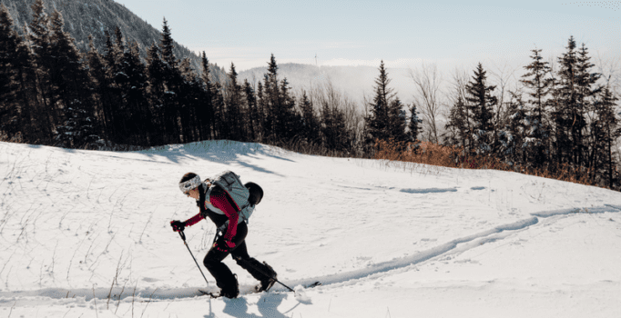 A person walks up a snowy slope in snowshoes on a sunny, winter day.