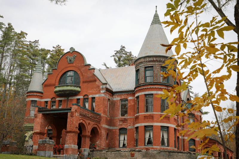 A large, red brick building is surrounded by trees with fall foliage.