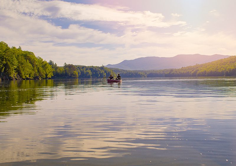 Two people in a canoe in the distance on a calm lake in the summer.