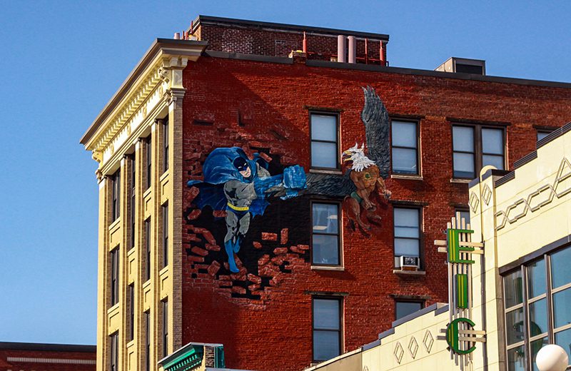 A painted mural of batman and a griffin on the side of a brick building.