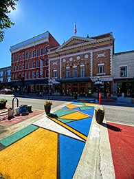 A colorful, geometric crosswalk on the street in front of a row of historic brick buildings.