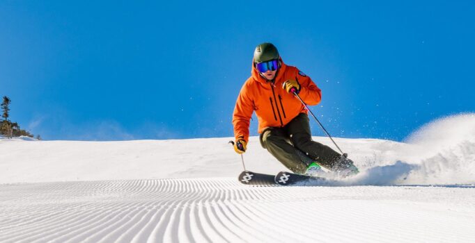 A person carves a turn on alpine skis down a groomed ski trail on a sunny day.