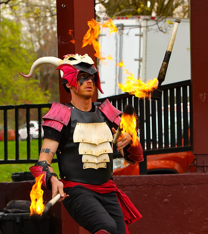 A person in costume twirls batons lit with fire.