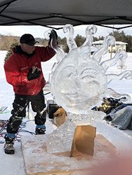 A person creates an ice carving outdoors at sunset.