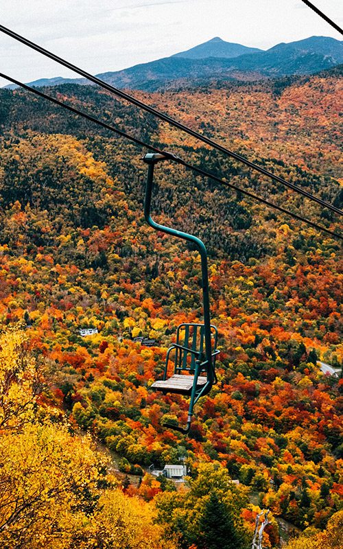 An empty ski lift moves above yellow, orange, and red trees.