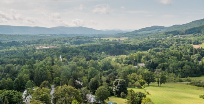 A landscape seen from above of patches of lush green trees and green mountains in the background.