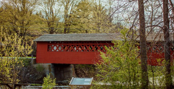 A red covered bridge spans a river in the spring.