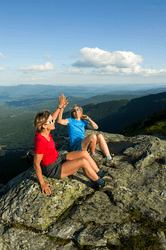 Two people high five on the top of an exposed mountain peak.