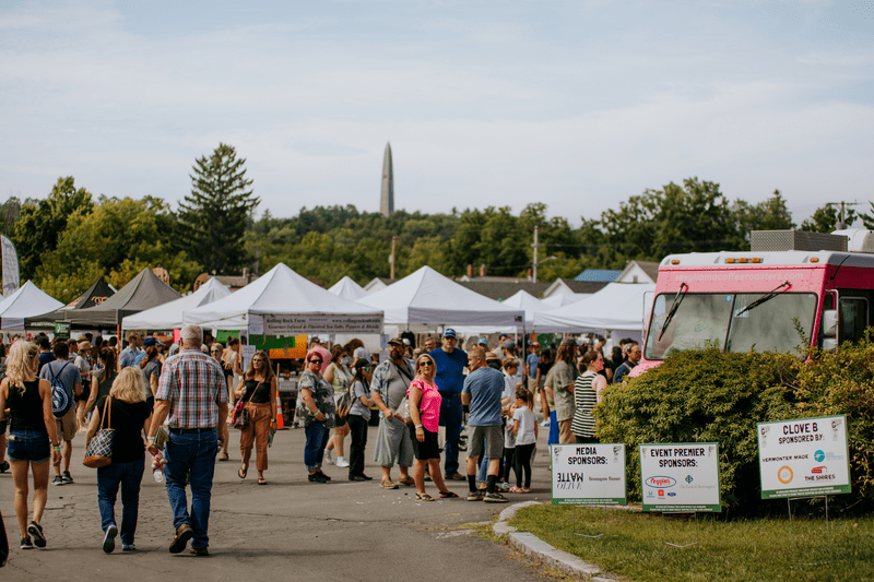 Crowds of people walk around at a festival with food trucks and tents.