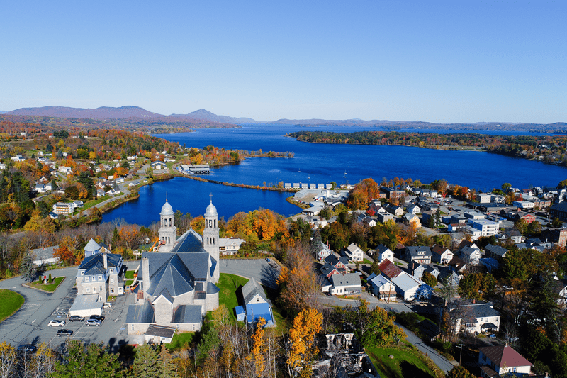 A view from above of downtown Newport that features a stone church in the foreground and a large blue lake in the background.