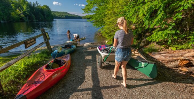 People load canoes into the water at a boat launch outside in summer.