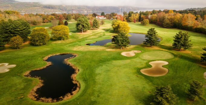 A golf course photographed from above in the early fall with rolling hills and colors on the leaves.
