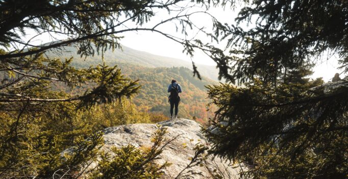 Seen from behind, a person takes in the view from a scenic overlook on a hiking trail.