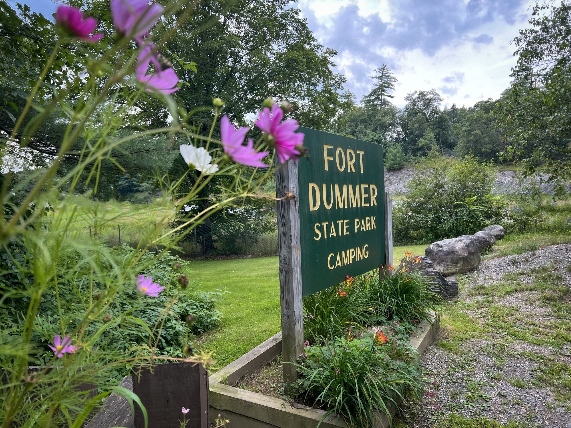 A sign reading “Fort Dummer State Park Camping” outside with flowers blooming in the summer.