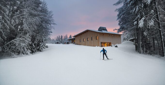 A person skis with a wooden building in the background.
