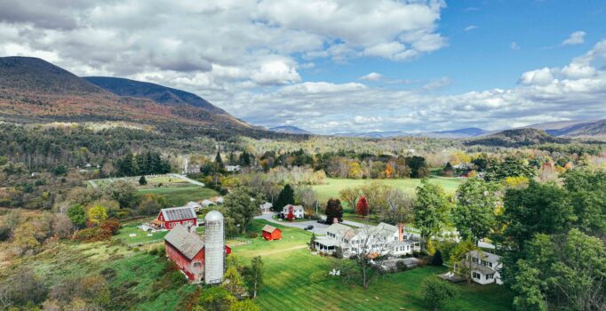 Seen from above, a red barn and several farm houses are nestled in a mountain valley.