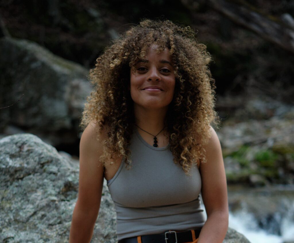 A person sitting on a rock smiles at the camera in this portrait-style image.