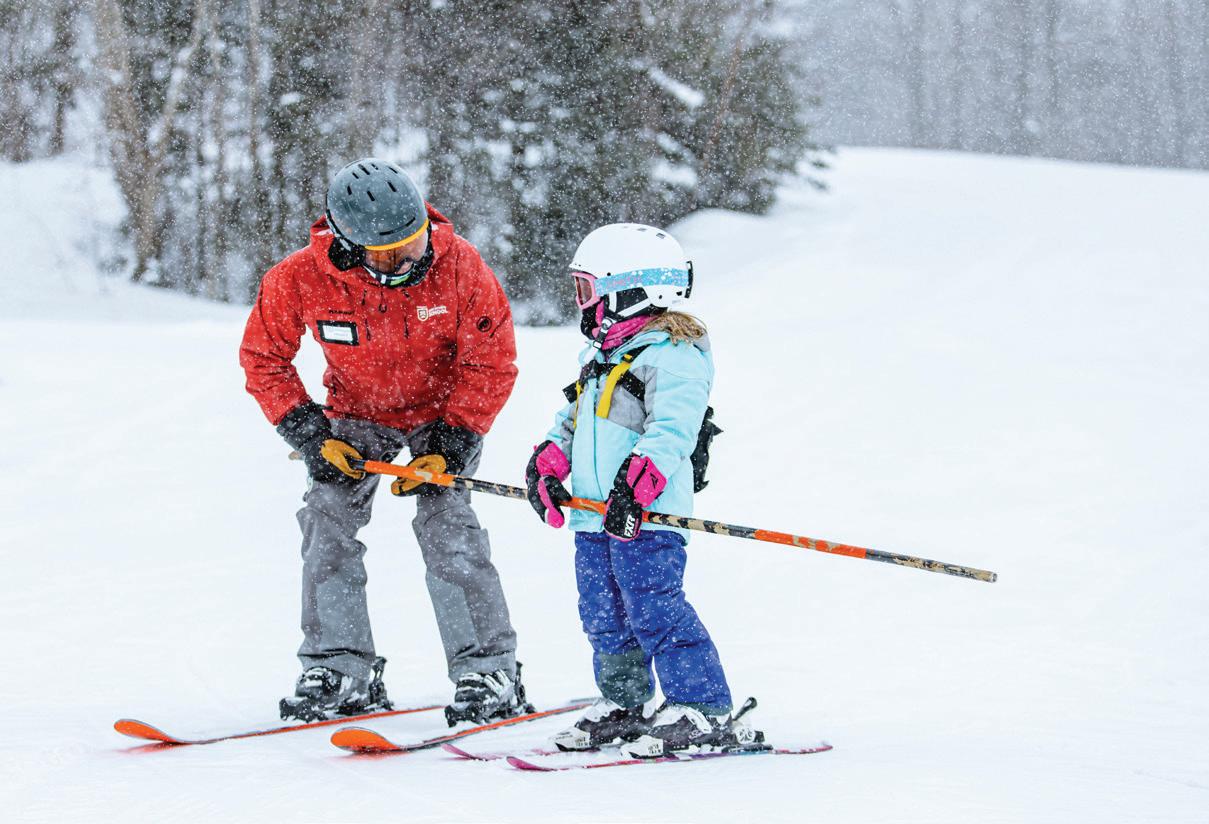 An adult and a child, both on skis, during a ski lesson outside in the winter. 