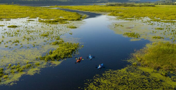 Ariel view of three kayakers paddling down a meandering river, surrounded by mountains.
