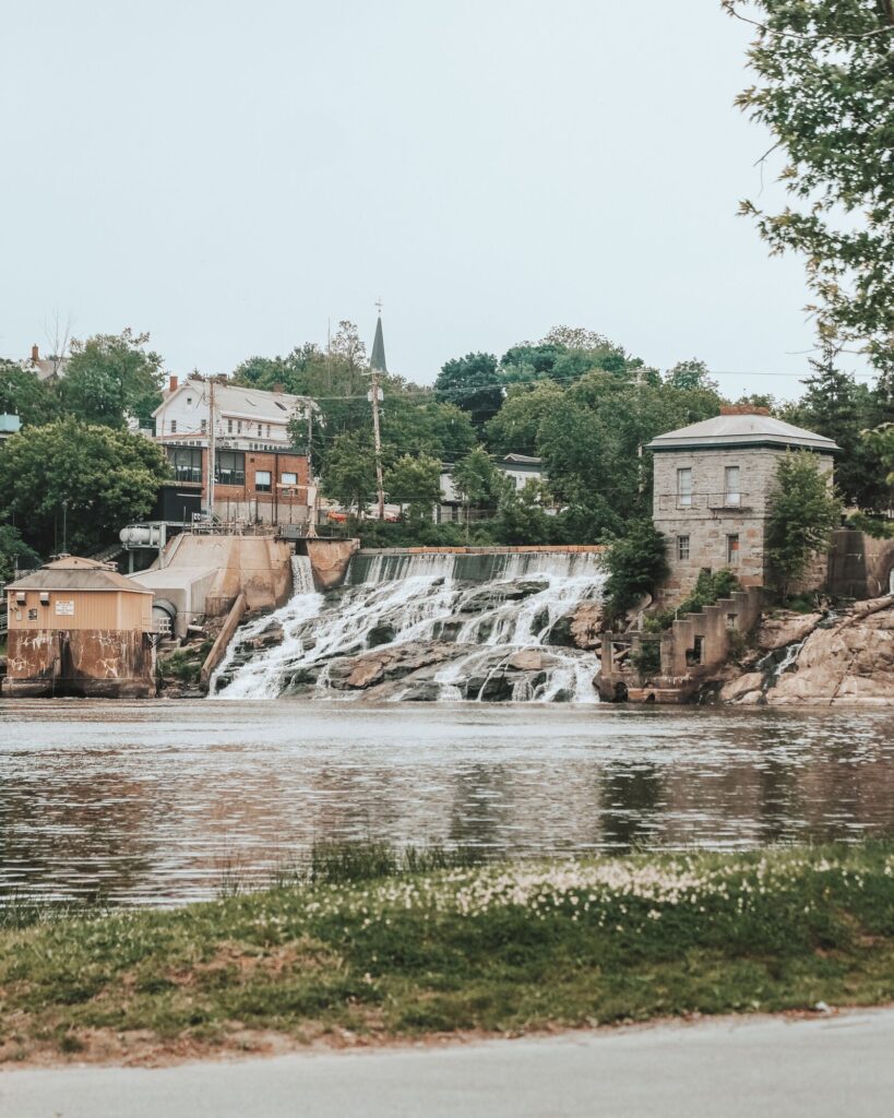 A waterfall seen from a distance with a historic downtown’s infrastructure surrounding it.