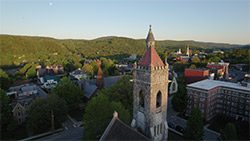 Seen from above, a historic downtown with a grey stone church nestled among mountains in the summer.