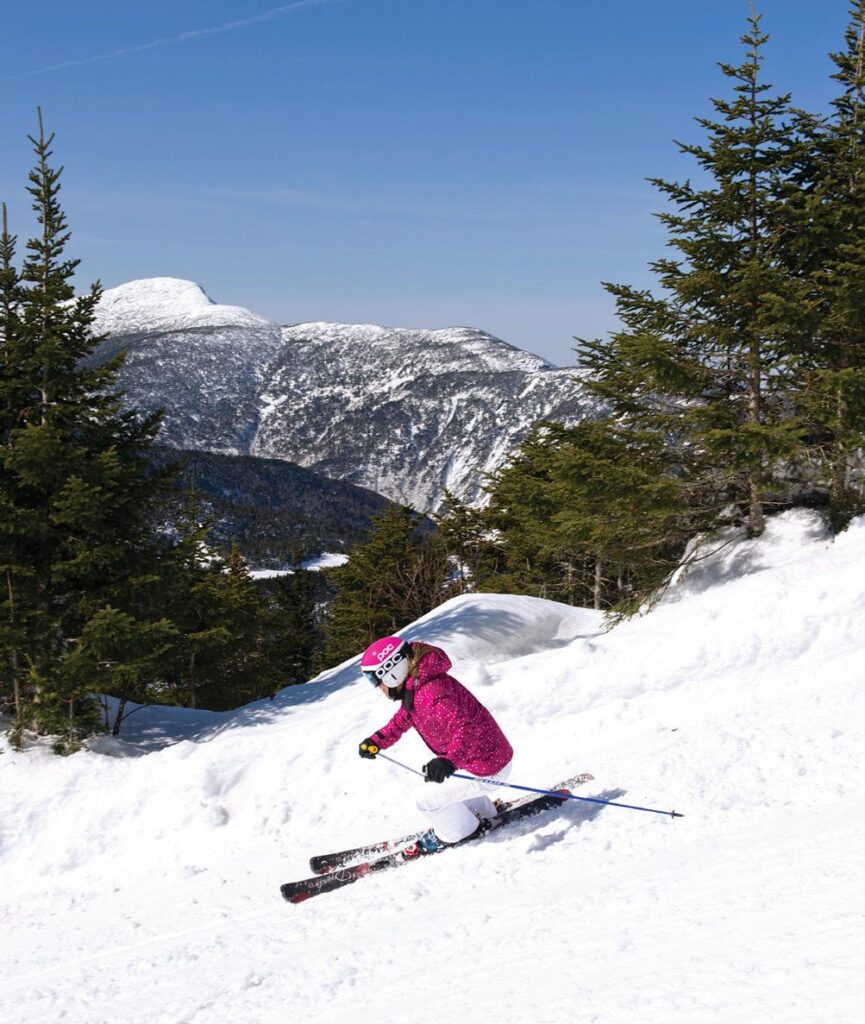 A person skis on a sunny day in the winter. A mountain is visible behind them.