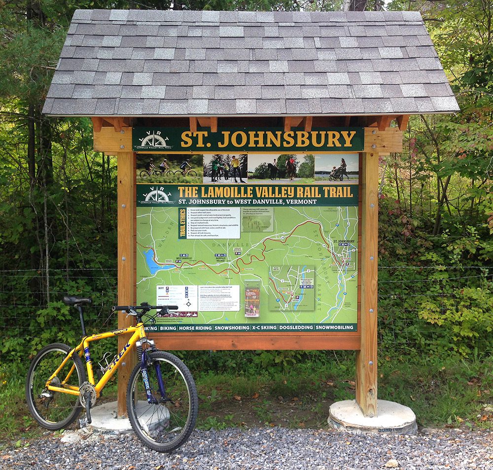 A yellow bicycle leans against a trail map that reads St. Johnsbury.