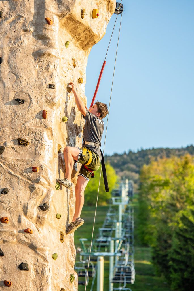 A person climbs up a rock wall outside in the summer.