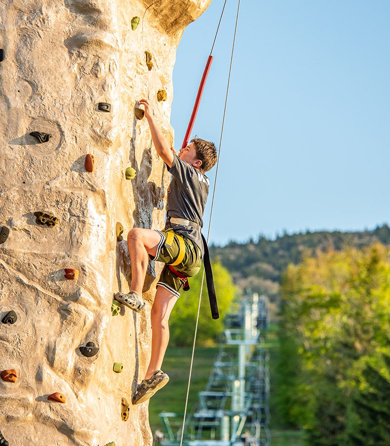 A person climbs up a rock wall outside in the summer.