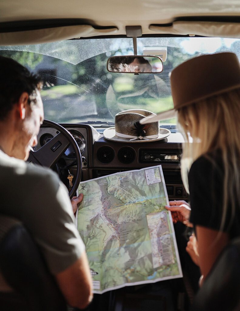 Two people seen from behind inside a car look at a map, seeming to plan their trip.