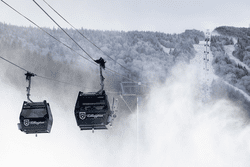 Two ski gondolas travel above snow making in the winter.