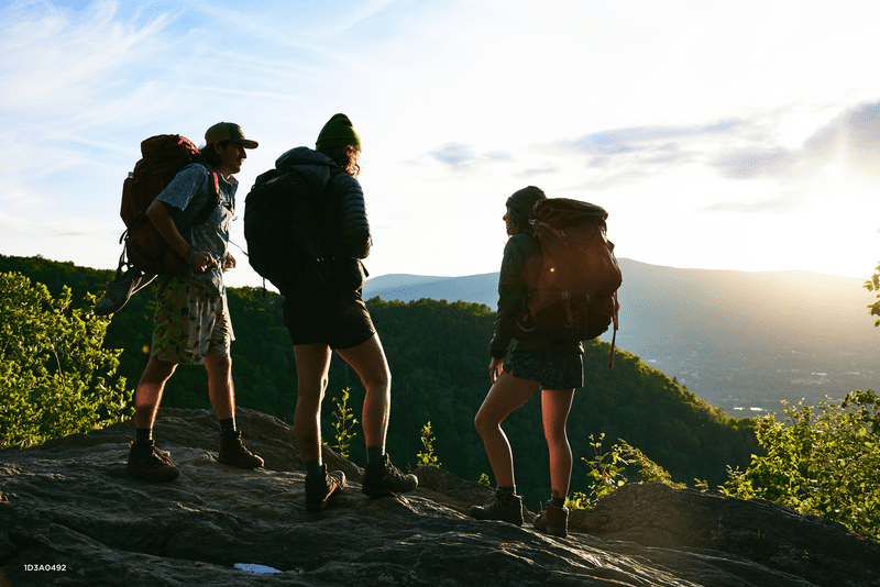 Three people stand with the sun behind them at a stone summit.