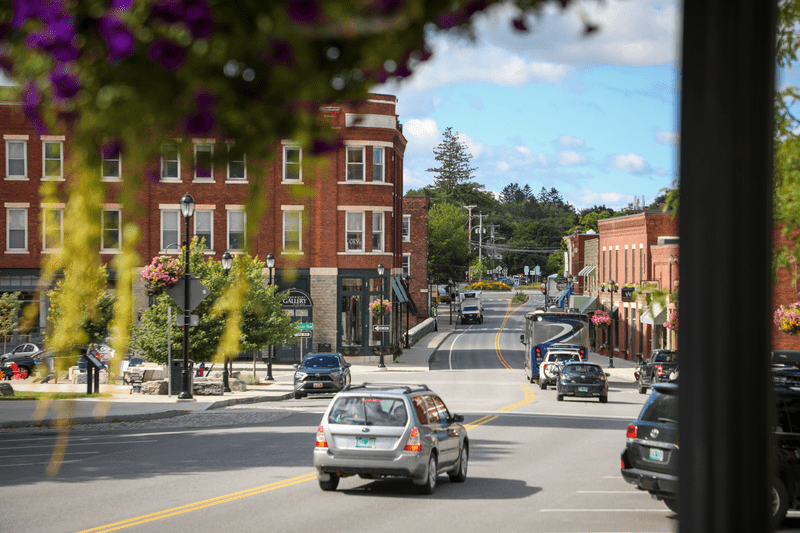 Cars drive along a historic downtown street with brick buildings lining both sides.