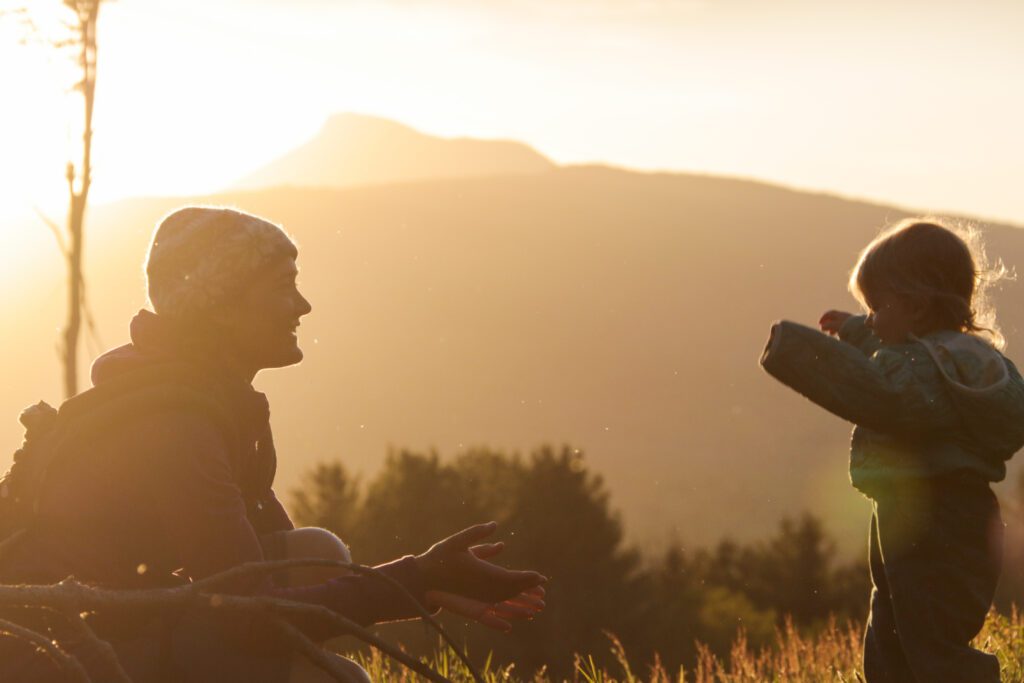 Parent embraces child hug with stunning backdrop of Camels Hump.