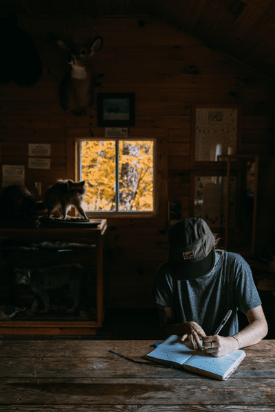 A person writes on a wooden table in a cabin.