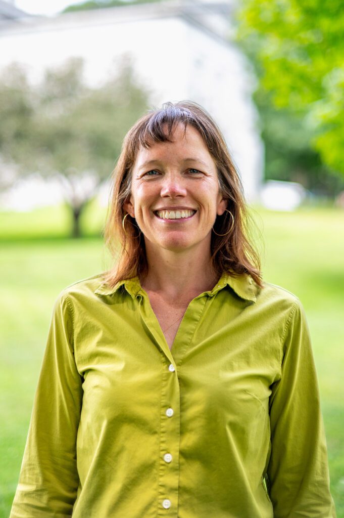 A person smiles at the camera wearing a green shirt outside on a sunny day.