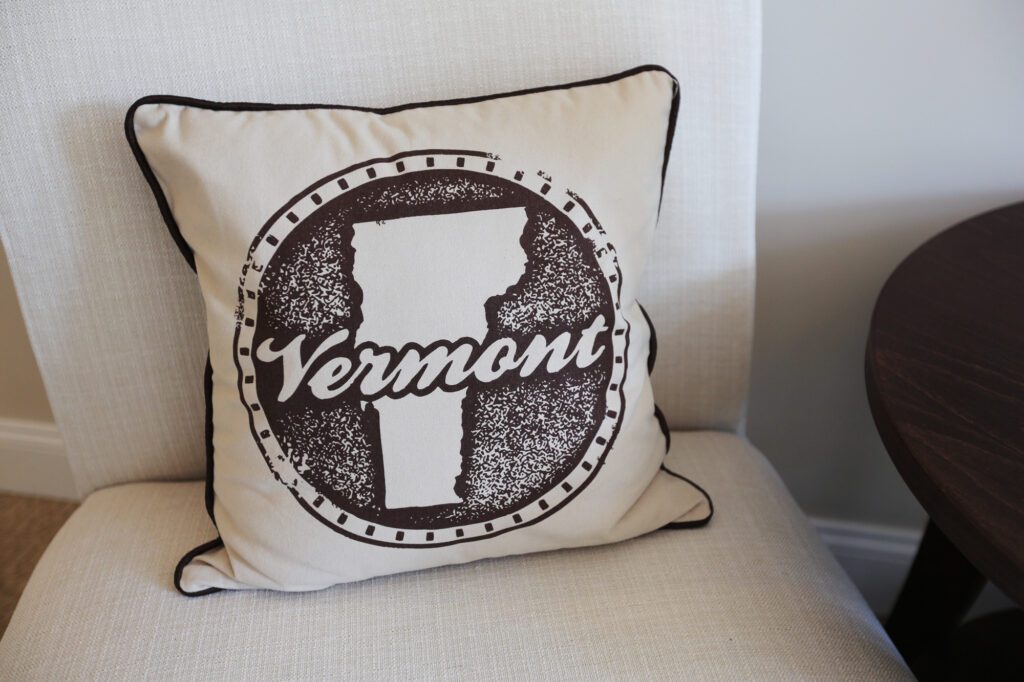 A chair with decorative pillow, presenting the work Vermont over the silhouette of the state.